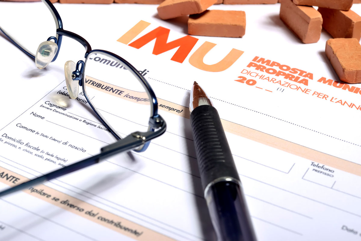 foglio di dichiarazione imu, paio di occhiali, penna e mattoncini